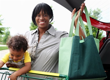 Black woman holding reusable shopping bags and toddler