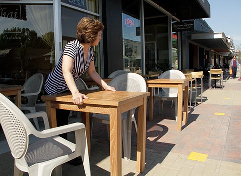 woman setting out tables in front of a Thai restaurant on Park Lane in preparation for its Grand Opening