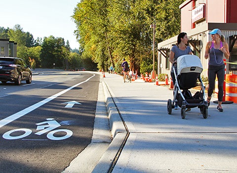 Two women walk on widened sidewalk next to bike lane on Market Street near Juanita Bay Park's boardwalk
