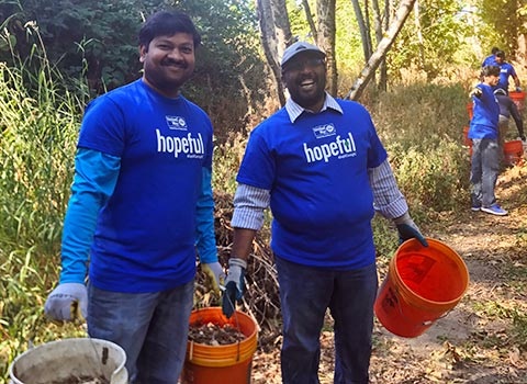 Indian men in blue hopeful shirts carrying mulch at a volunteer restoration event