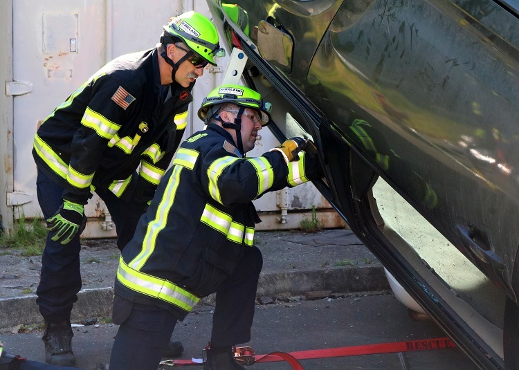 Two firefighters looking at an upended vehicle