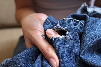 putting a finger through a hole in ripped jeans