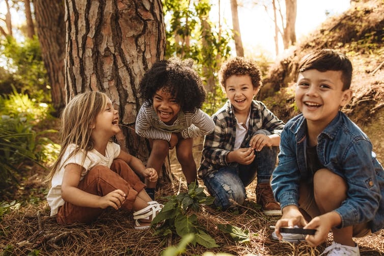 Children sitting and laughing near a tree trunk
