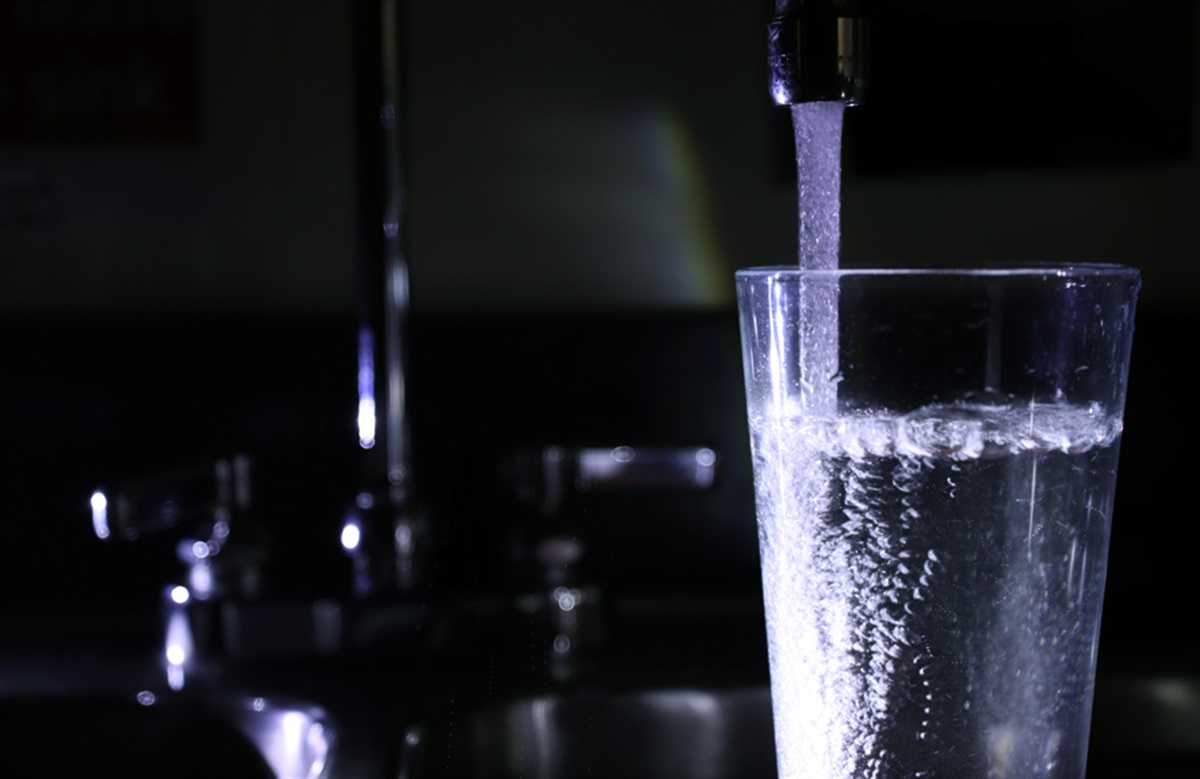 A faucet filling a glass with water.